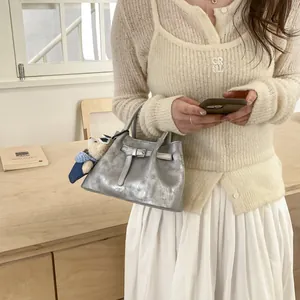 Detail of silver metallic bucket bag with belt decor and cute bear sunglasses charm