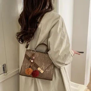 Detail of brown crossbody bag with vertical textures and a decorative fluffy pompom charm