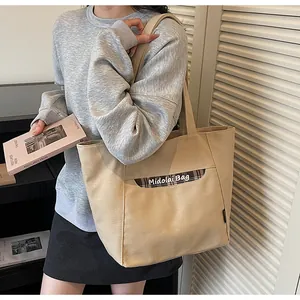 Dettaglio della borsa tote in tela con tasca frontale, bordo a quadri marroni e tessuto beige