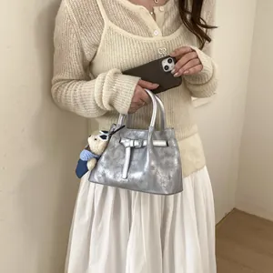 Detail of silver bucket bag featuring distressed texture and a cute teddy bear charm