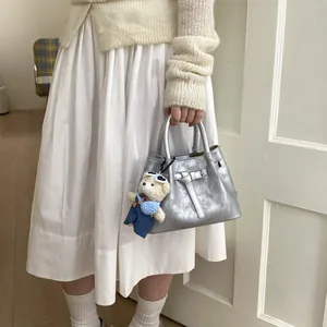 Detail of silver metallic bucket bag with belt decor and cute white teddy bear charm