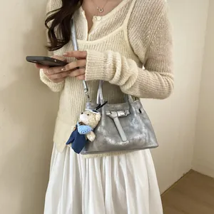 Close-up of metallic silver bucket bag featuring a decorative belt and teddy bear charm