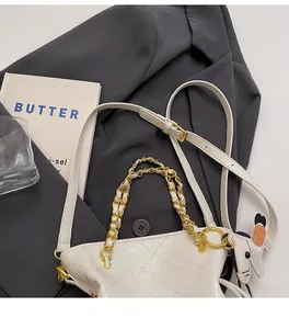 Detail view of a white quilted bucket bag with golden chain handle and a small dog charm