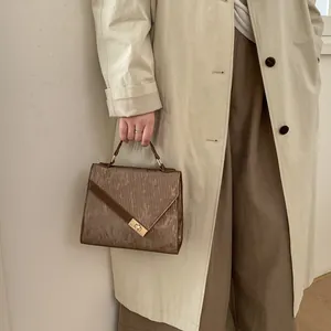 Detail of brown pleated square handbag with golden metal twist lock and leather strap