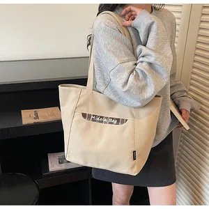 Dettaglio della borsa tote in tela beige con tasca a quadri e tracolla larga