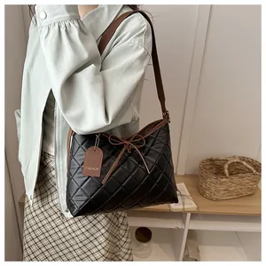 Detail of a black quilted shoulder bag with bow decor and a leather fashion tag accessory