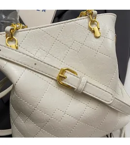Detail of white quilted leather bucket bag with adjustable gold chain strap and buckle