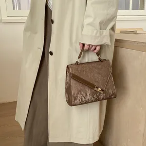 Detail of a brown small square bag with metallic texture and gold clasp on a beige coat
