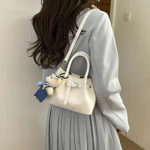 Chic cream bucket bag with belt decor and cute bear charm shown on a fashion model back view