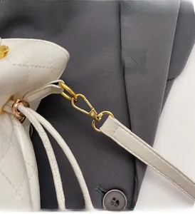 Detailed macro of golden hardware clasps on white quilted bucket bag with chain strap