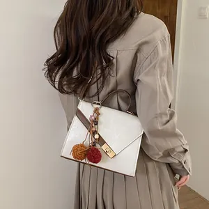 White leather handbag with gold lock and colorful pompom detail on model's shoulder