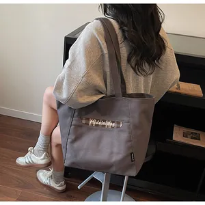 Dettaglio borsa tote in tela grigio scuro con ricamo a scacchi indossata sulla schiena