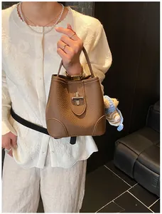 Detail of brown lychee grain leather bucket bag with silver lock and cute bear charm