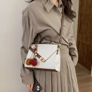 Chic pearl white crossbody bag with brown trim and plush charm worn by a model