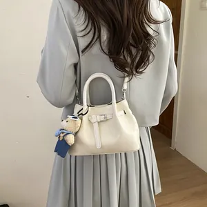 Close-up of beige bucket bag with belt detail, top handles and cute bear charm pendant