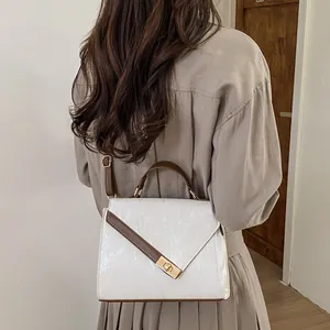 Beige leather crossbody bag with brown trim and gold buckle shown on a model
