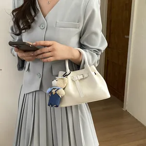Close-up of cream bucket bag with decorative belt strap and cute plush bear charm accessory