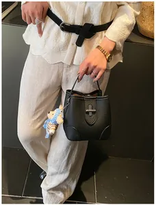 Detail of black lychee leather bucket bag with metal turn-lock and cute bear charm