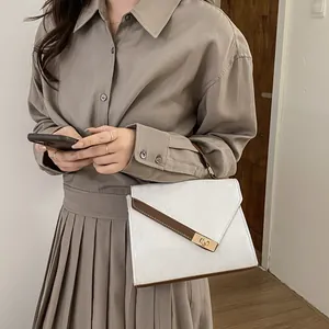 Detail of white and brown crossbody bag featuring a modern golden rectangular twist lock