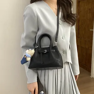 Detail of a black bucket bag with leather texture, belt decor and plush bear charm