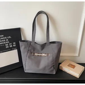 Dettaglio della borsa tote in tela grigia con patchwork a quadri marroni e ricamo bianco