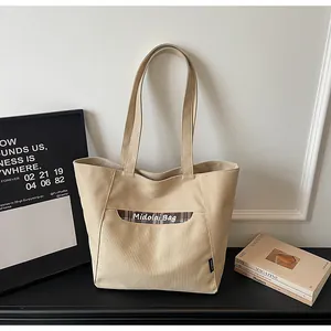 Dettaglio borsa tote in tela beige con tasca a quadri marroni e scritte artistiche