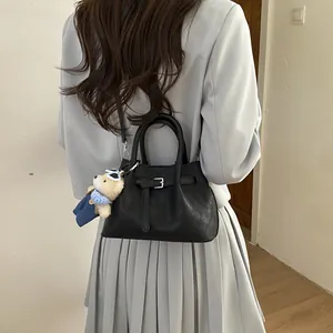 Detail view of a black bucket bag with a belt buckle and a small teddy bear pendant charm