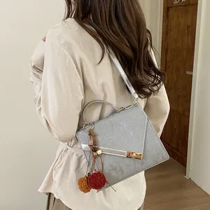 Detailed side view of grey textured mini square bag with golden lock and pompom charm