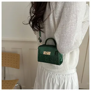 Detail of dark green textured handbag with gold lock on a model in a casual setting