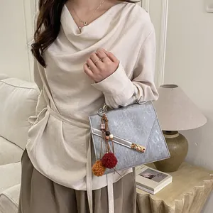 Detail view of silver square handbag with gold rotary lock and colorful tassel pendant