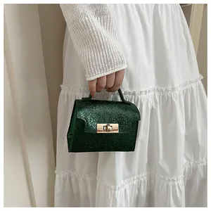 Detail of dark green snake-textured handbag with gold metallic twist lock closure
