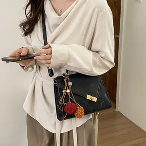 Detail of black textured crossbody bag with golden clasp and bohemian tassel charm