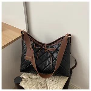 Detail of quilted leather tote bag with brown bow charm and metallic tag decoration