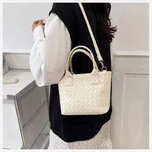 Detail of cream woven leather bucket bag with top handles and adjustable gold-tone strap