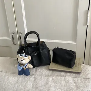 Detail of black leather bucket bag with belt decor and a cute teddy bear charm