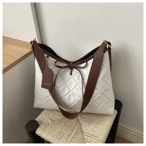 Close-up of white quilted tote bag featuring brown leather bow and fashion tag detail