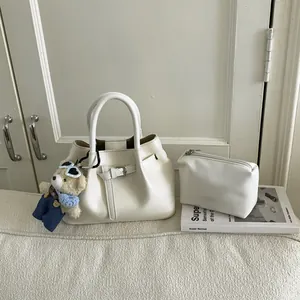 White leather bucket bag with inner pouch and a cute bear keychain on a beige sofa