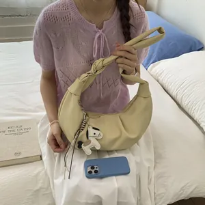 Detail einer cremefarbenen Halbmond-Tasche mit geknotetem Riemen und kleinem Pferdeanhänger