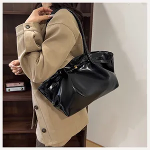 Détail du sac seau en cuir verni noir avec boucle dorée et design plissé élégant