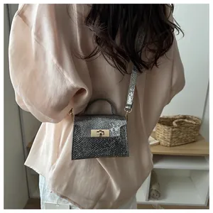 Detail of silver snakeskin textured handbag with gold lock carried by model