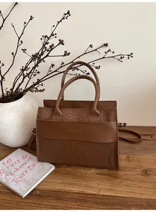 Dettaglio di una borsa marrone con motivo a coccodrillo, trama a serpente e manici rotondi