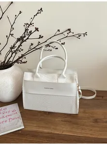 Dettaglio della borsa bianca con trama a coccodrillo e scritte su un tavolo minimalista