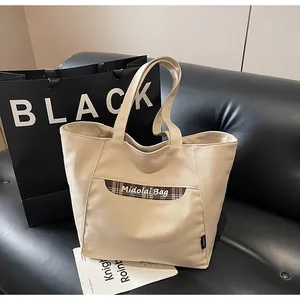 Dettaglio della borsa tote in tela beige con tasca a quadri blu e ricamo