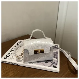 Detailed view of silver textured small square bag with golden twist lock on desk