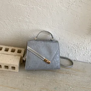 Detail of silver textured handbag featuring gold rectangular twist lock and top handle