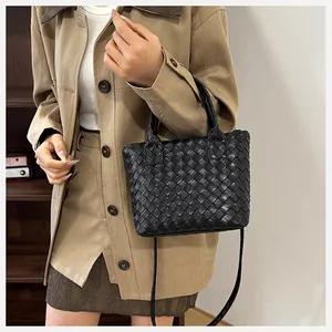 Detail of black woven leather handbag with top handle and crossbody strap on shoulder