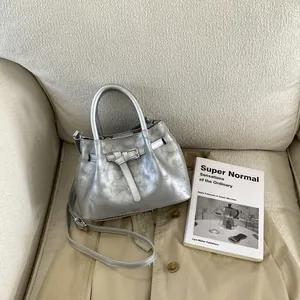 Detail of silver pleated bucket bag with metallic texture and strap on a beige trench coat
