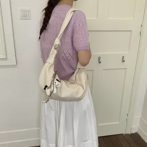 Detail der cremefarbenen Hobo-Tasche mit geknotetem Gurt und Welpenanhänger
