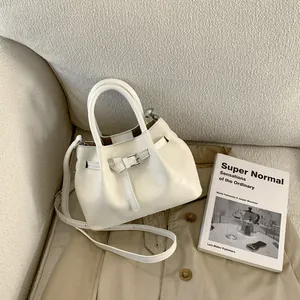 Detailed view of cream PU leather bucket bag with decorative belt buckle on a sofa