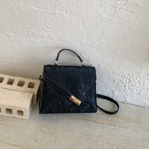 Detail view of black corduroy handbag with gold twist lock on ivory brick background